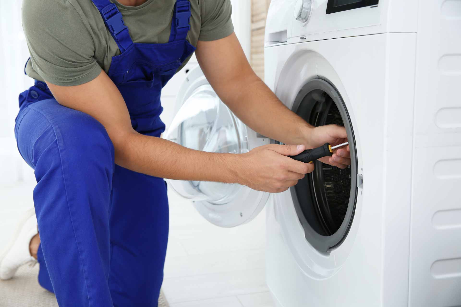 Appliance repair technician kneeling to repair a washer/dryer