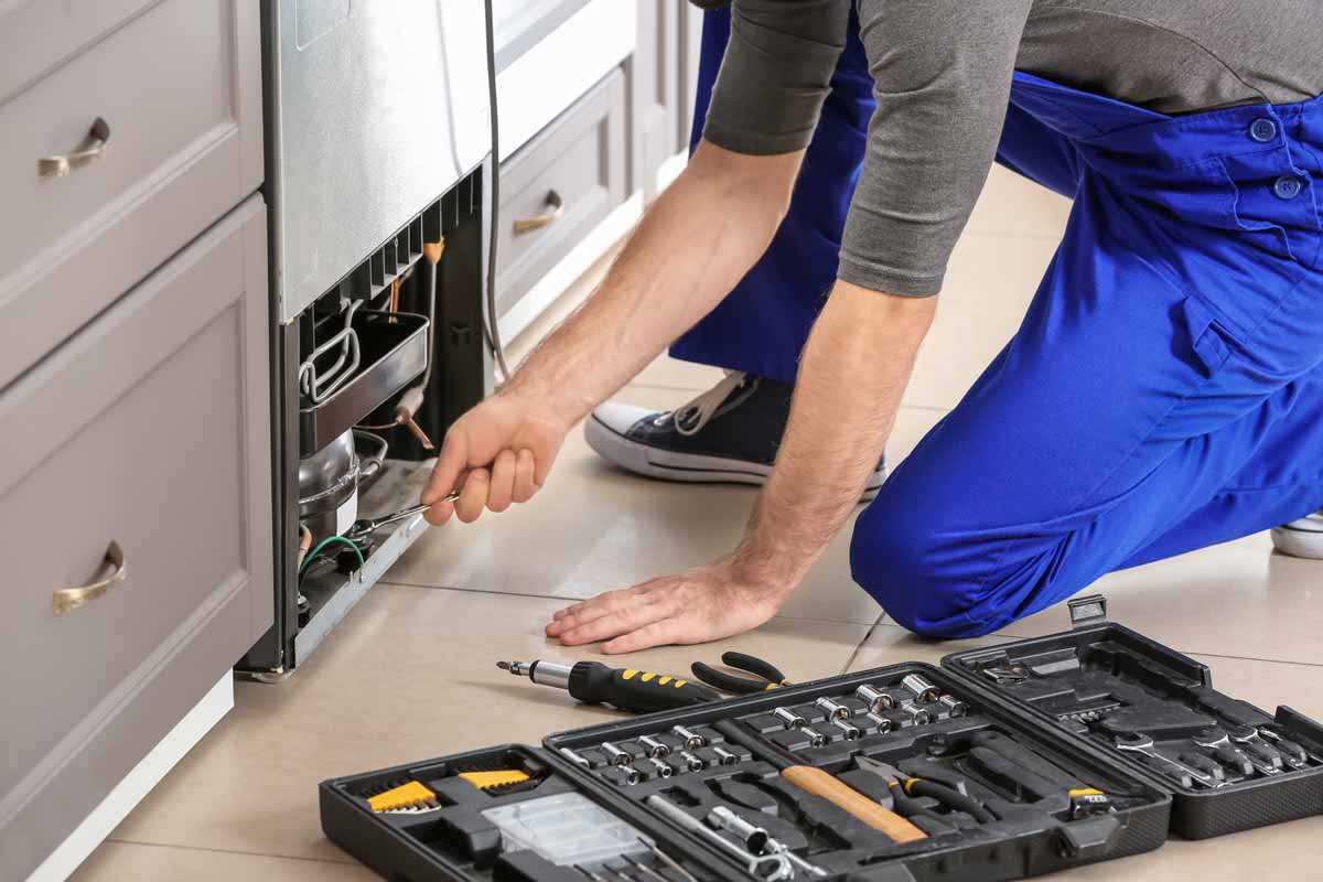 Man kneeling to repair a refrigerator